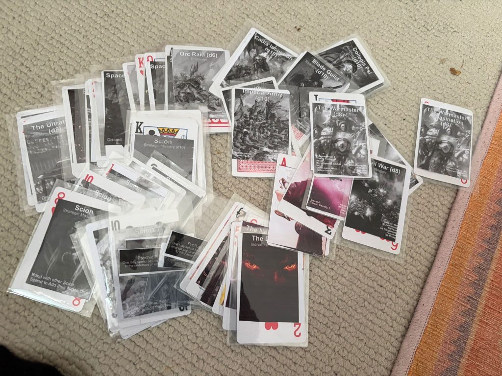 My physical deck of The Scions cards, spread on a dirty carpet with a rug. The "card protectors over cards, and then you can swap stuffs" is something I learned from Jay Dragon. Thanks, Jay!